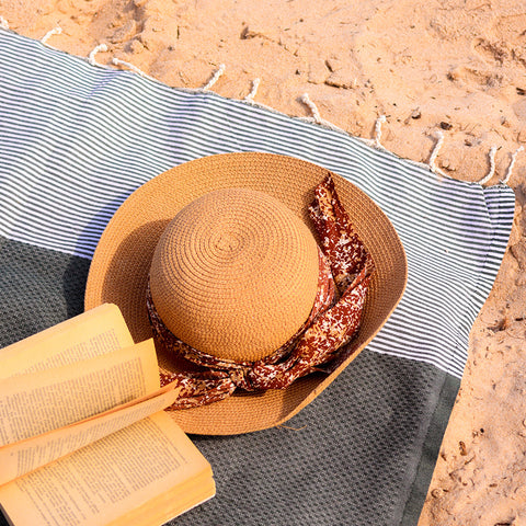 ein Buch und ein Hut auf einem dunkelgrauen Hamamtuch Strandtuch am Strand