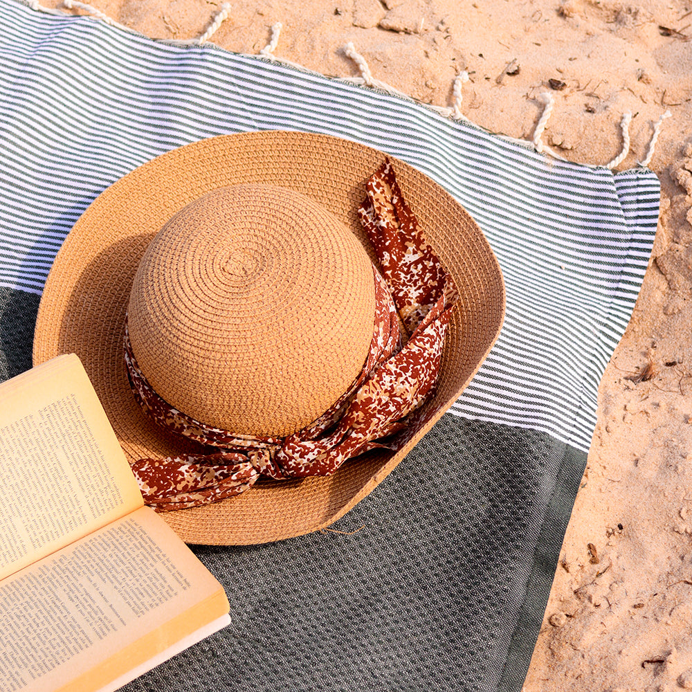 ein Buch und ein Hut auf einem dunkelgrauen Strandtuch fouta am Strand