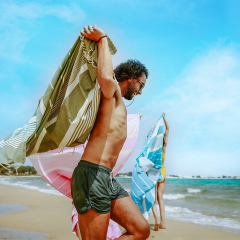 eine Gruppe von Freunden am Strand die jeweils ein farbiges Strandtuch fouta halten