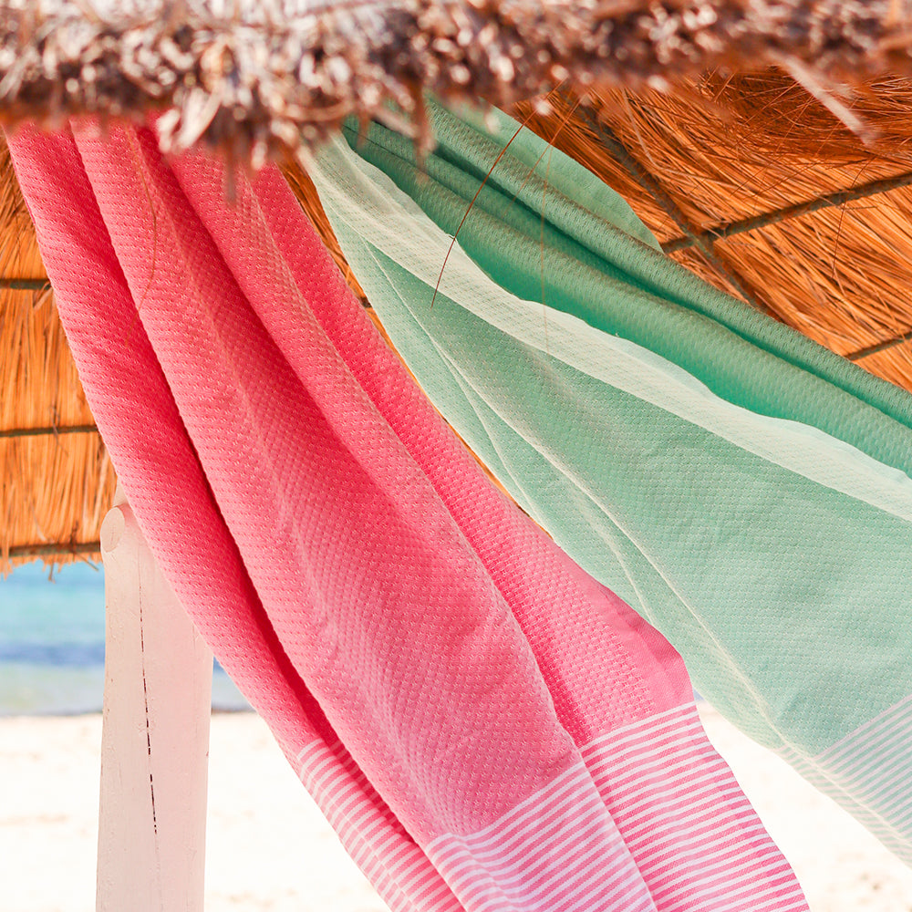 eine rosafarbene Fouta und ein aquablaues Strandtuch hingen unter dem Sonnenschirm