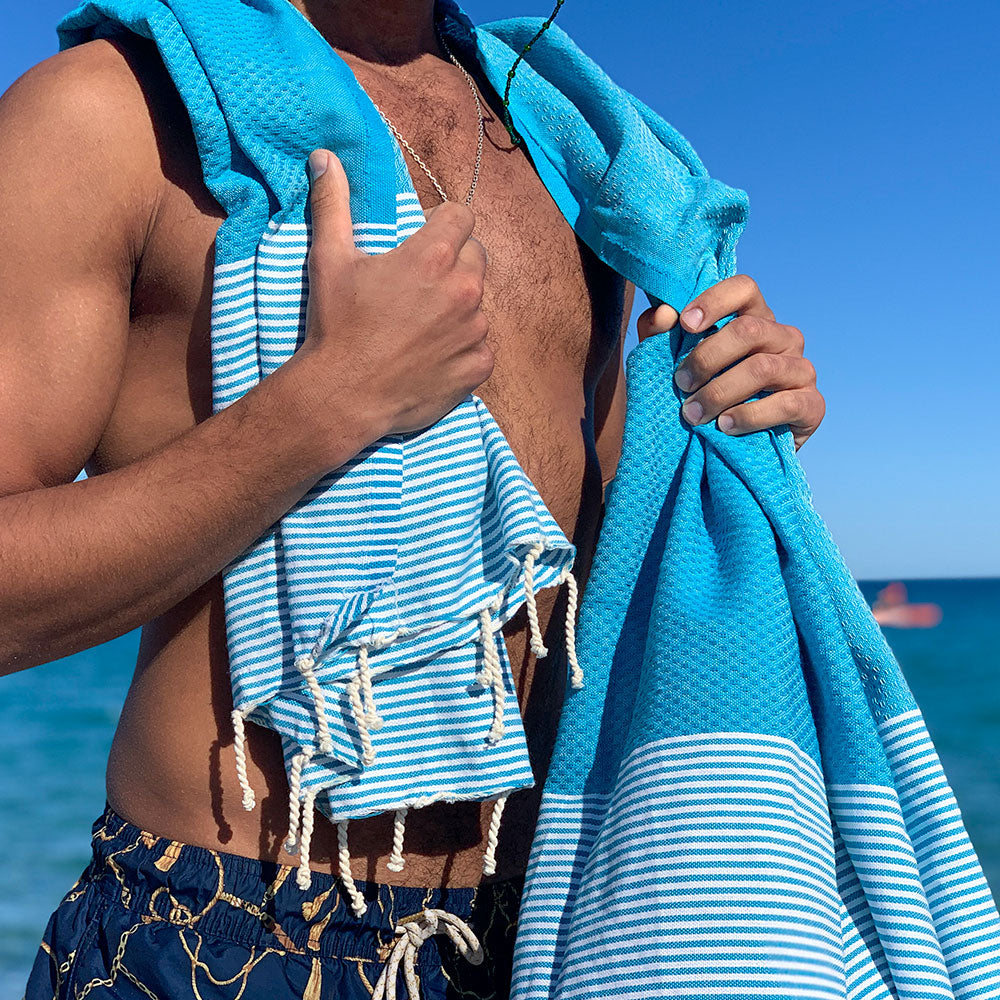 Mann mit aquablauem Strandtuch fouta auf den Schultern am Strand