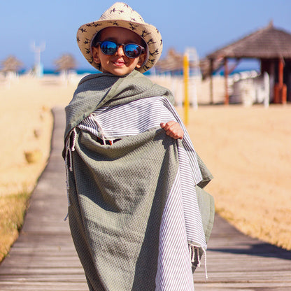 Kind am Strand mit Hut und Sonnenbrille in braunem Strandtuch