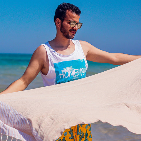 Mann hält ein Hamamtuch fouta in beige am Strand