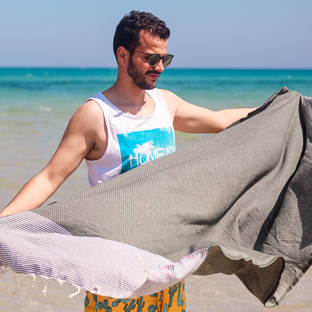 Ein Mann am Strand, der ein braunes Hamamtuch hält 