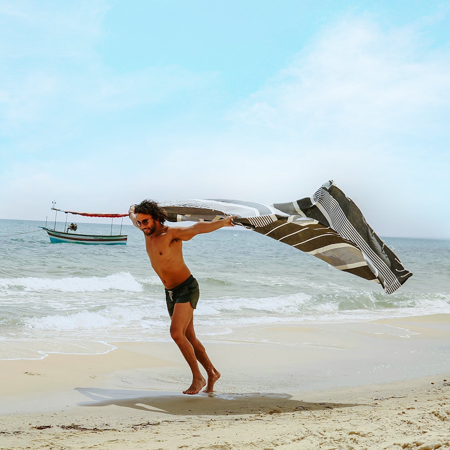 Mann am Strand der ein platingraues hamamtuch fouta hält