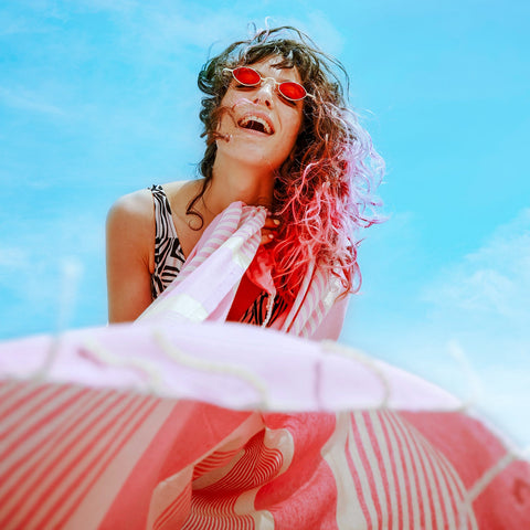 ein Mädchen mit Sonnenbrille das ein rosa Strandtuch fouta hält