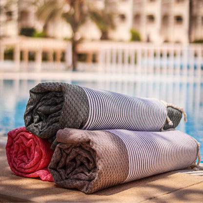 ein gefaltetes Fouta Strandtuch in Korallenrosa, Braun und Grau, das am Pool hängt