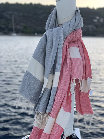 ein blaues Strandtuch und eine rosa Fouta die um eine Bootsstange gewickelt ist