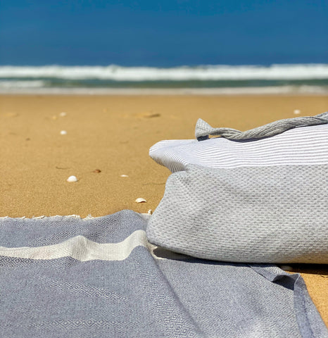 graues Strandtuch fouta und Strandtasche im Sand