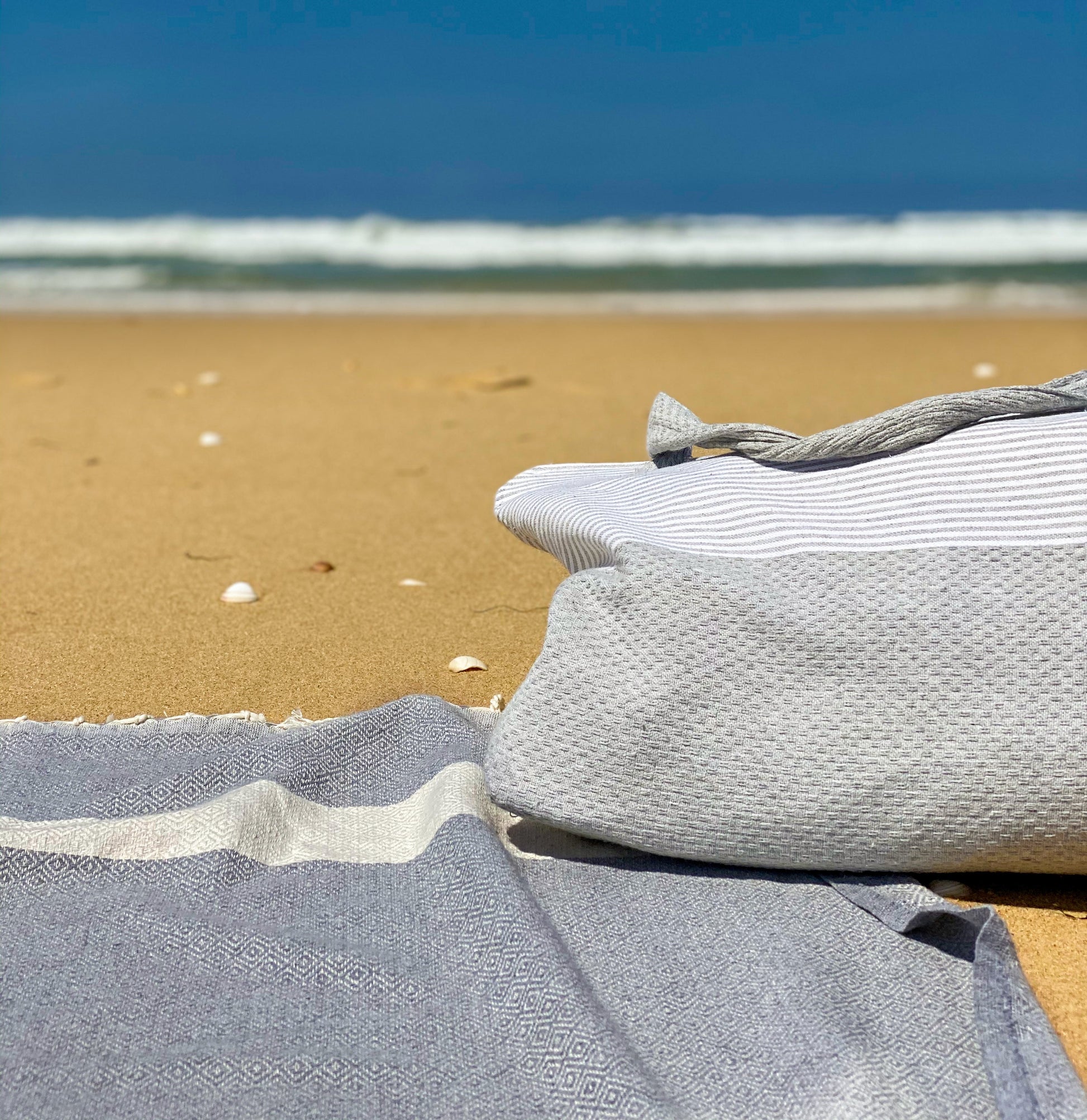 ein dunkelgraues Hamamtuch und eine Strandtasche im Sand