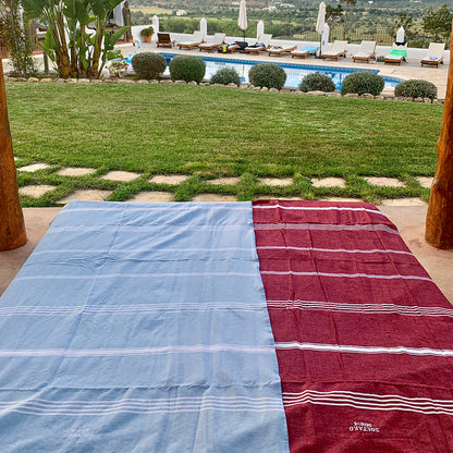 ein dunkelrotes Strandtuch und eine hellblaue Fouta am Swimmingpool