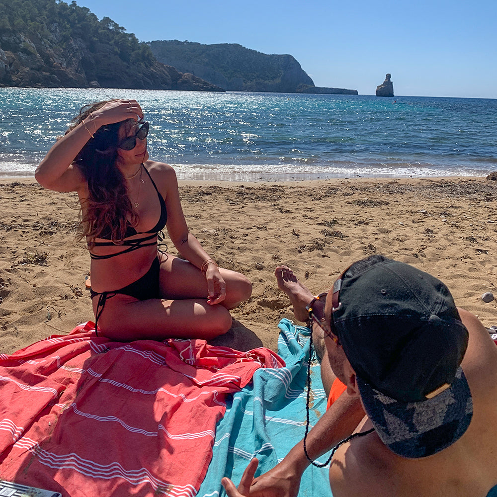 Paar auf einer hellblauen Fouta und einem rosa Strandtuch am Strand liegend