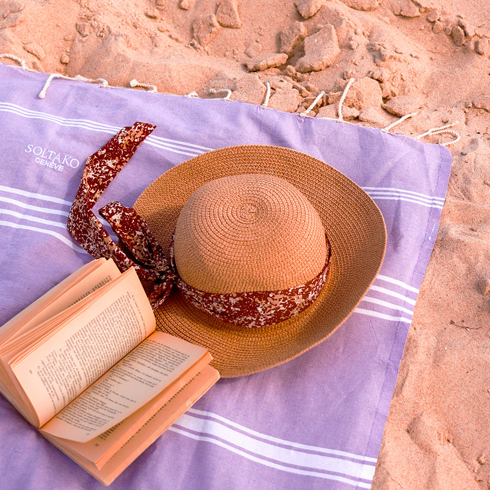 ein Buch und ein Hut auf einem hellgrauen Hamamtuch im Sand