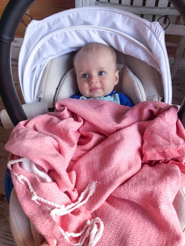 Baby in der Babyschale, bedeckt mit einem korallenrosa Strandtuch